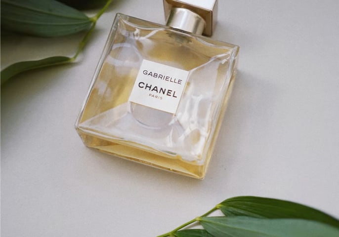 Bottle of Chanel perfumes on a light background, surrounded by green leaves